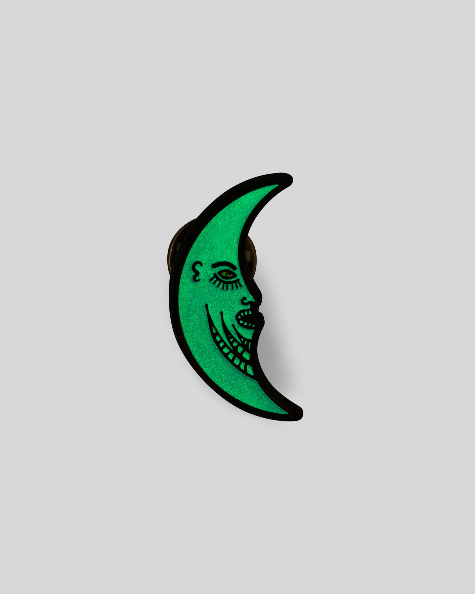 1987 Half Moon Pin. Blue metal half moon face pin showcasing glow in the dark green.